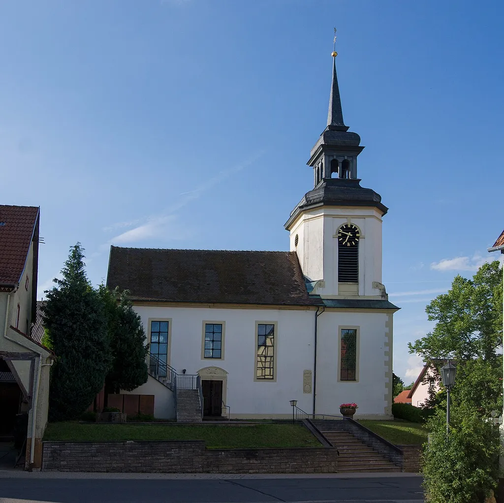 Die Südseite der Evangelische Kirche von Buch am Ahorn. Kirchturm mit Uhr. Rechts der Kirche eine Hecke.