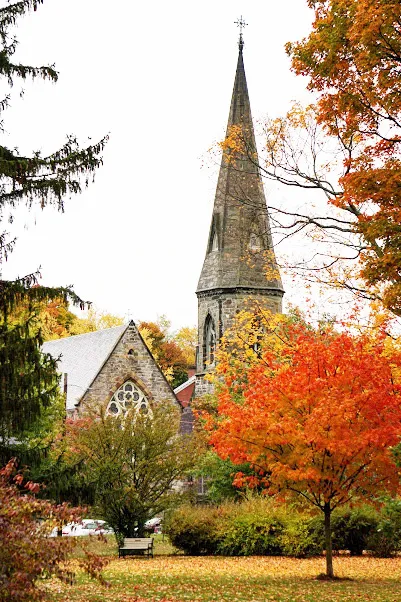 The stone tower and spire of Grace Church, Newton, as viewed from Farlow Park during autumn.