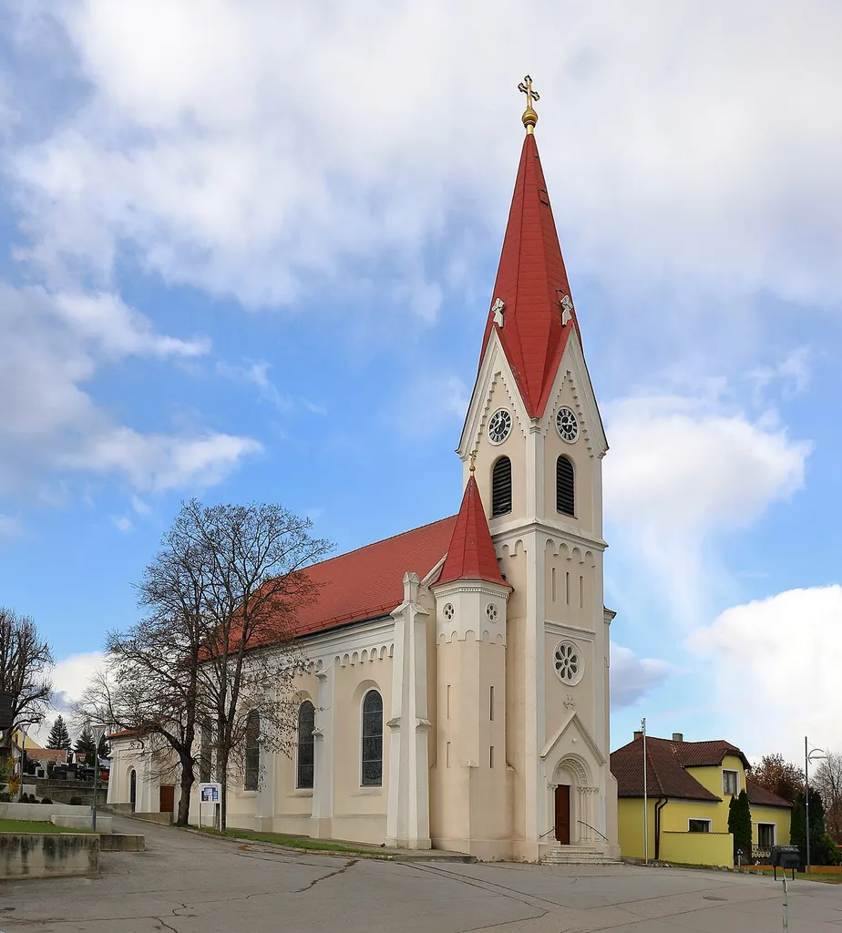 Südostansicht der röm.-kath. Pfarrkirche hl. Nikolaus in der burgenländischen Gemeinde Nickelsdorf.Die Kirche wurde ein wenig nördlich anstelle einer vor 1572 erbauten, zu kleinen und baufälligen Kirche ab 1904 errichtet und am 15. Oktober 1905 geweiht. Sie hat ein vierjochiges Langhaus mit Strebpfeilern, einen Ostturm, einen Treppenturm und einen eingezogenen Chor.