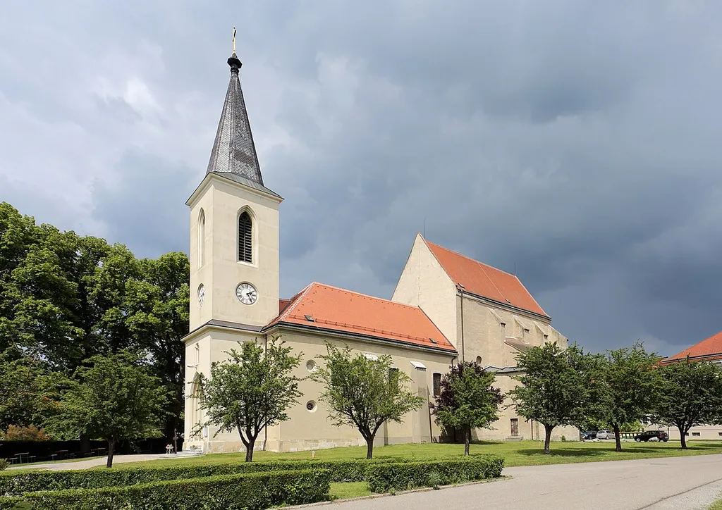 Südwestansicht der Pfarrkirche hl. Margaretha der niederösterreichischen Stadt Marchegg. Der mächtige, mehrfach veränderter Sakralbau mit dominierendem frühgotischem Chor aus dem 3. Viertel des 13. Jahrhundert war ursprünglich von einem Friedhof umgeben und befindet sich in der Stadtmitte. Die Kirche war 1268 als große dreischiffige Stadtpfarrkirche konzipiert. Nach schweren Zerstörungen durch den ersten österreichischen Türkenkrieg 1529 und 1634 (Schwedenkrieg) wurde nur der Chorbau als Kirche verwendet. Unter Karl Fürst Pálffy errichtete man 1789/90 das wesentlich kleinere Langhaus. Der zweigeschossige Westturm mit steilem Spitzhelm wurde 1855 errichtet.
