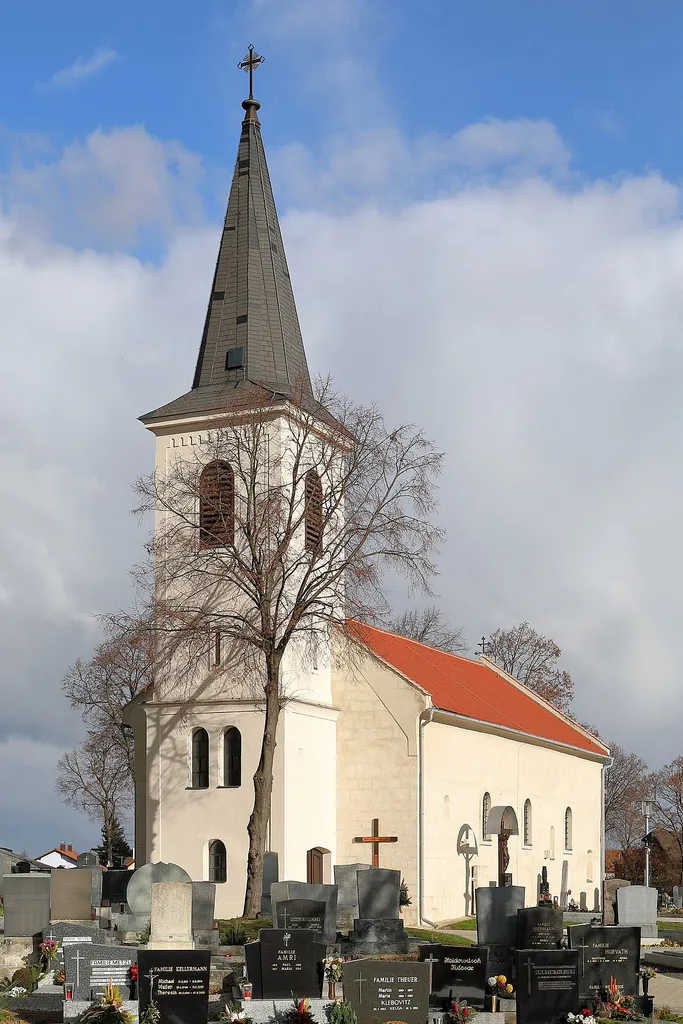 Südwestansicht der röm.-kath. Pfarrkirche Hll. Petrus und Paulus in der burgenländischen Marktgemeinde Zurndorf.Eine im Kern romanische-frühgotische Saalkirche in erhöhter Lage, die von einem Friedhof umgeben ist. Der zweigeschossige, vorgestellte West wurde nach einem Brand 1857 wiederinstandgesetzt bzw. neu errichtet.