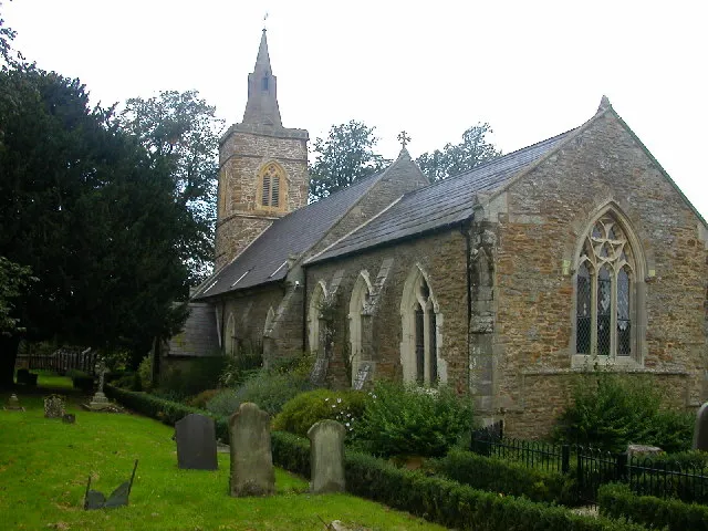 Clay Coton. Formerly St Andrew's church built in 1340, disused since the 1950s, now converted into a very large house. A public footpath runs through the centre of the picture and the grounds are a mixture of garden and gravestones.