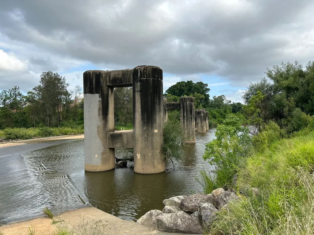 The former Liverpool Footbridge was accessed from Newbridge Road on the eastern side of the George's River or from Lighthorse Park on the western side of the River. The pylons are all that remain of the original railway bridge structure. The bridge is a substantial structure at a considerable height over the watercourse. It consists of a series of large cylindrical concrete posts embedded in the George's River. Supported by the posts was a metal-grid frame with a wooden base that formed a public walkway, however some time after the railway was dismantled, in around 2007 the pedestrian bridge was dismantled due to concerns for its structural integrity. Text adapted from the NSW Heritage Listing item which is licensed under CC-BY-4.0.
