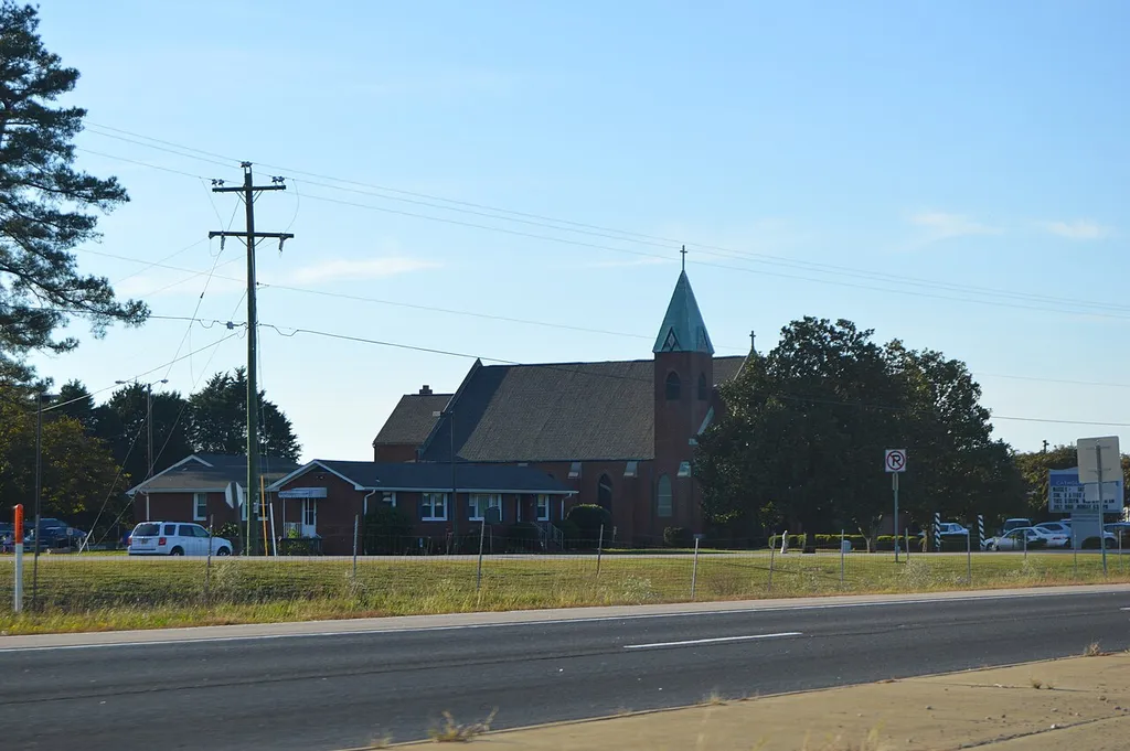 Distant view from the west of Sacred Heart Catholic Church, located along U.S. Route 460 at 9300 Community Lane, just southeast of Petersburg, in Prince George County, Virginia, United States. Built in 1906, it is listed on the National Register of Historic Places.