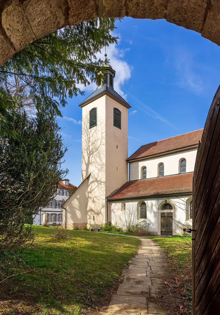 Bad Boll (Landkreis Göppingen): Stiftskirche St. Cyriakus (oft nach Berta von Boll Bertakirche genannt), eine dreischiffige romanische flachgedeckte Pfeilerbasilika aus dem 12. Jahrhundert. Ansicht von Südosten durch das einzige erhaltene Tor der ehemaligen Ummauerung des Kirchenareals.