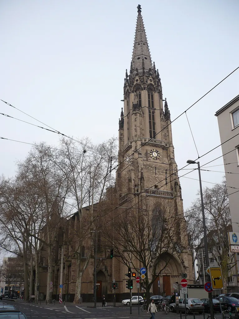 Herz-Jesu-Kirche, Köln, Zülpicher Platz; Blick von der Zülpicher Straße entlang der Nordfassade der Kirche zum Ring. Der Turm der Kirche ist nach den Türmen des de:Kölner Doms der höchste Kirchturm der Stadt. Die gegen Ende des 19 Jh errichtete neugotische Kirche wurde im Zweiten Weltkrieg weitgehend zerstört und nur teilweise stilerhaltend und grundrißgleich wiedererbaut.