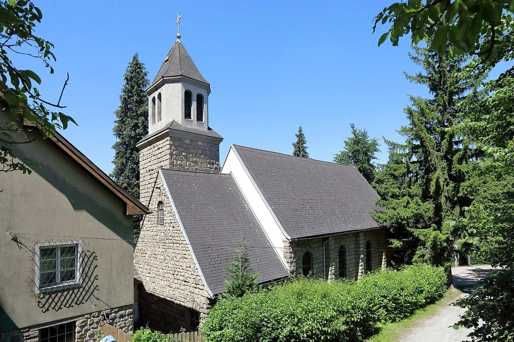 Ostansicht der Dollfuß-Gedächtniskirche hl. Theresia vom Kinde Jesu in Rekawinkel, ein Ortsteil der niederösterreichischen Stadtgemeinde Pressbaum. Der freistehende Kleinkirchenbau mit eingezogenem niedrigerem Chor und südlichem Chorwinkelturm wurde ab Herbst 1933 errichtet und am 20. Oktober 1935 von Kardinal Theodor Innitzer geweiht. 1951 erfolgte die Erhöhung des Turmes und chorseitig der Pfarrhof errichtet. 1952 wurde Rekawinkel eine eigenständige Pfarre. Auf Grund der Zusammenlegung der Pfarren Pressbaum und Rekawinkel mit Wirkung vom 1. September 2024 ist die Kirche seit damals eine Filialkirche ohne eigene Rechtspersönlichkeit der römisch-katholischen Pfarre Pressbaum.