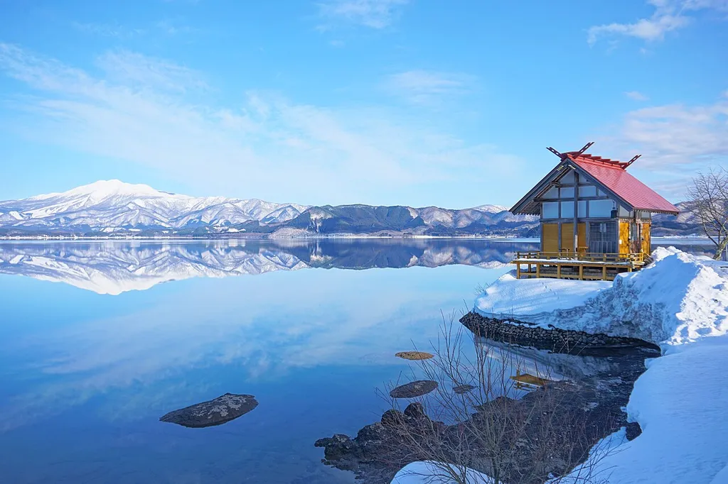 Kansaki Palace stands on Lake Tazawa &amp; the lakeside, &amp; beyond the lake, there’s a distant view of Mt. Akita Komagatake (Semboku City, in Akita Prefecture).