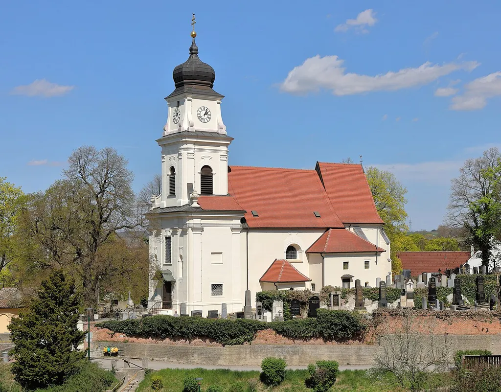Südwestansicht der röm.-kath. Pfarrkirche hl. Johannes der Täufer in der niederösterreichischen Marktgemeinde Bisamberg.Die Kirche steht erhöht über dem Ort am nordwestlichen Abhang des Bisamberges und ist von einem Friedhof umgeben. Sie ist eine im Kern romanische, barockisierte Saalkirche mit spätgotischem Chor und spätbarockem Westturm. Der tiefe Fassadenvorbau mit Turm wurde von 1720 bis 1735 errichtet.