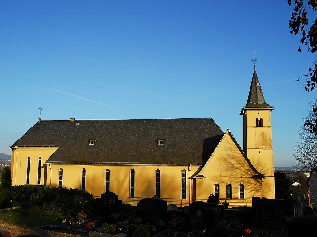 Katholische Pfarrkirche Hl. Dreikönige in Kempten am Rhein (Bingen am Rhein), Dreikönigstraße 4: Saalbau, im Kern vermutlich spätkarolingisch, romanische Umbauten sowie solche des 16. Jahrhunderts, barocke Überformung im 18. Jahrhundert, Erweiterung 1933, Architekten Ludwig Becker und Anton Falkowski, Mainz; Turm romanisch, Spitzhelm 19. Jahrhundert; ortsbildprägend. Ansicht von Westen.