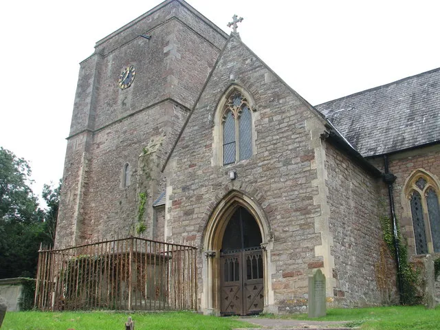 West tower and south porch of SS Mary and Peter, Tidenham, Gloucestershire, seen from the east. On the left enclosed by railings is the Madocke family tomb, probably installed in 1736. See inscription on the northwest side of the tomb, facing the south porch: 542114.