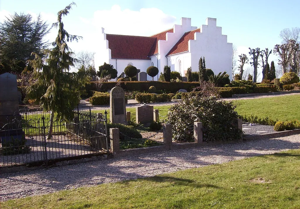 Flade Church in Frederikshavn municipality, Denmark, is situated on high ground, and therefore it has been of importance for navigation, just as the whole coast be observed from here. The church was built in a Roman style in the early 13th century, and it has never had a tower. The choir and the nave are the oldest parts whereas the porch is from the late Middle Ages. A chapel was added about 1675. In the church yard there are two ancient mounds, on one of which the bell frame of the church is placed. Many places around the country it’s possible to find the churches situated next to grave mounds from ancient time and today there is some dissension as the importance of this.
