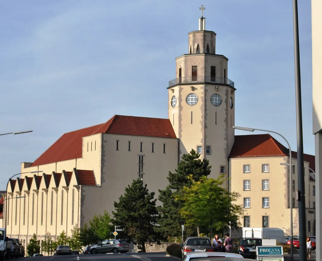 Katholische Herz-Jesu-Kirche, Wandpfeilerkirche mit erhöhtem Mittelschiff und eingezogenem flachen Dreiseitchor, oktogonaler Turm mit zwei sich stufig verjüngenden Obergeschossen seitlich neben Portalfassade, Walmdächer über Mittelschiff und westwerkartiger Portalfassade, Zwerchhausreihung über Seitenschiffen, Putzfassade mit Kalksteinkanten und -rahmungen über hohem unverputztem Sockelgeschoss, Expressionismus, Albert Boßlet, 1927/28; mit Ausstattung