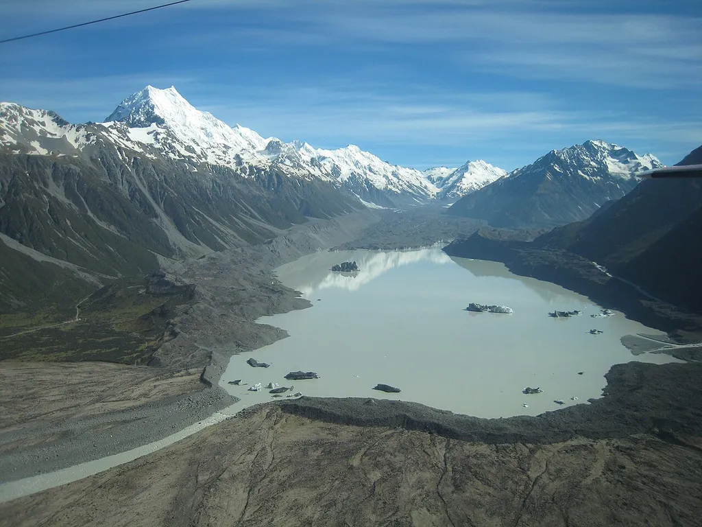 Aerial view of New Zealand's Tasman Lake, surrounded by the Tasman Glacier and its moraines. Aoraki/Mount Cook is behind on the left. The plane's tail can be seen on the right, and a guy wire is visible in the upper left.