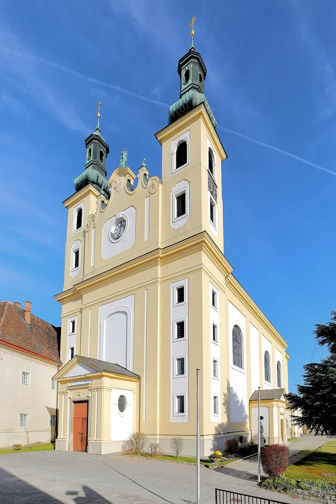 Südwestansicht der Pfarr- und Wallfahrtskirche zur Schmerzhaften Mutter Gottes in der niederösterreichischen Gemeinde Maria-Lanzendorf.Die Kirche mit einer Doppelturmfassade wurde unter Einbeziehung der älteren Gnadenkapelle (gotischer Chor der Vorgängerkirche) von 1699 bis 1703 durch den Baumeister Franz Jänggl errichtet. Von 1723 bis 1731 wurde die Kirche nach Osten hin um einen von einer mächtigen Kuppel gekrönten Chorraum, erweitert, wodurch die Gnadenkapelle jetzt innerhalb des Langhauses platziert ist.