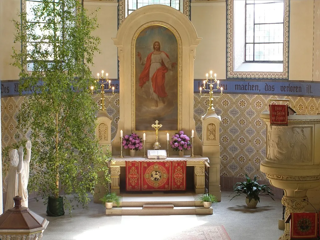 Altarraum der Lutherkirche Chemnitz-Harthau, pfingstlich geschmückt, links Taufstein, Christusfigur, Pfingstgrün, Mitte: Altar mit Altarbild aus Magdeborn, rechts: Kanzel und Lesepult