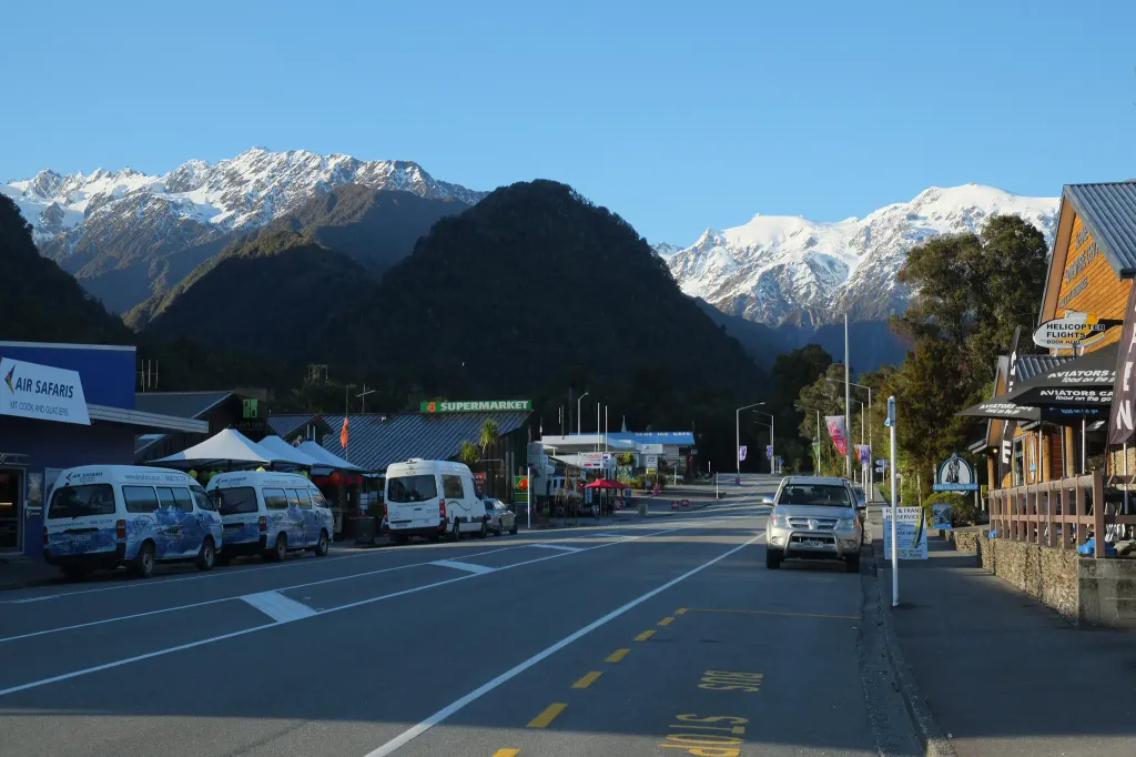 Main street of Franz Josef in the morning with snow-covered Baird Range and Fritz Range in the background