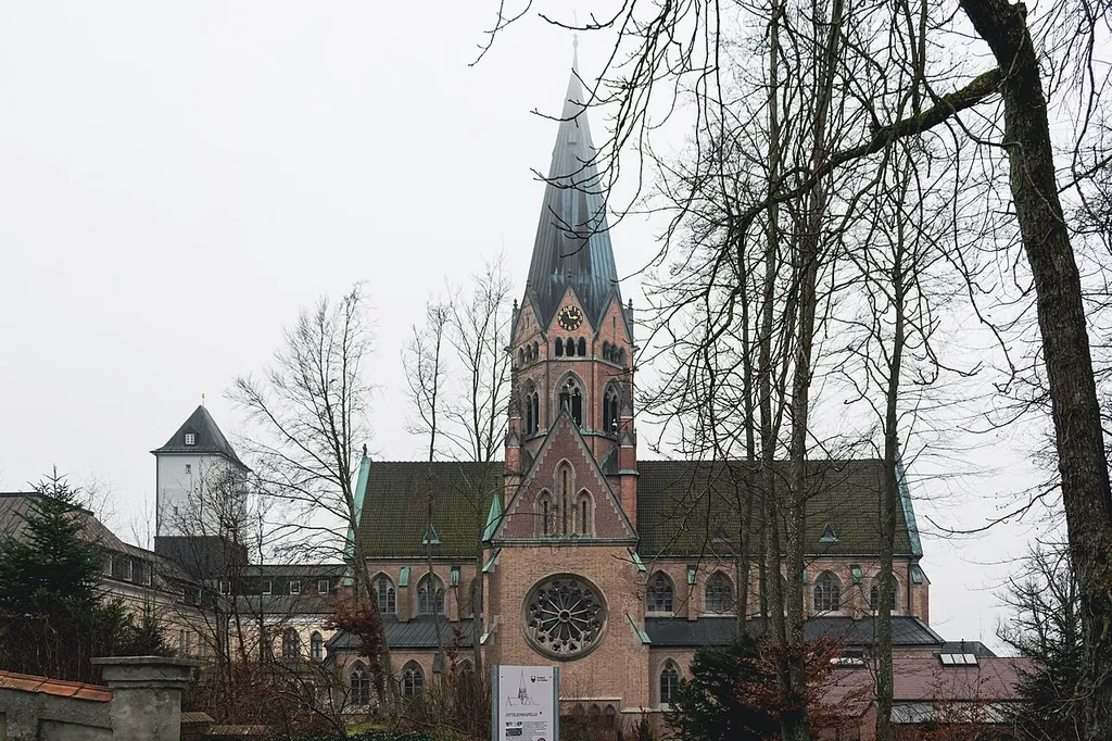 The monastery church St. Ottilien on a foggy day. Only the silhouette of the cross on top of its tower are visible.