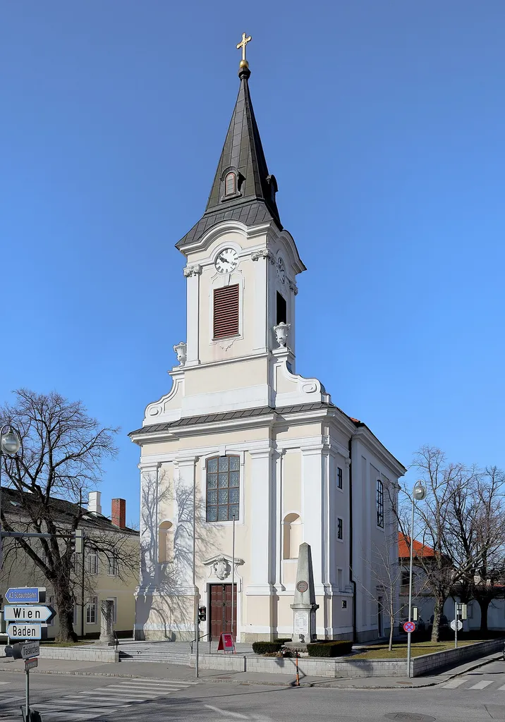 Ostansicht der röm.-kath. Pfarrkirche hl. Wolfgang in Tribuswinkel, ein Ortsteil der niederösterreichischen Stadtgemeinde Traiskirchen.Nachdem die Vorgängerkirche durch einen Brand zerstört wurde, erfolgte 1732 ein Neubau in Form einer barocken Saalkirche nach Plänen des Hofarchitekten Anton Marinelli. Bei einem neuerlichen Brand 1877 wurde der barocke Turmhelm durch einen Pyramidenhelm ersetzt.