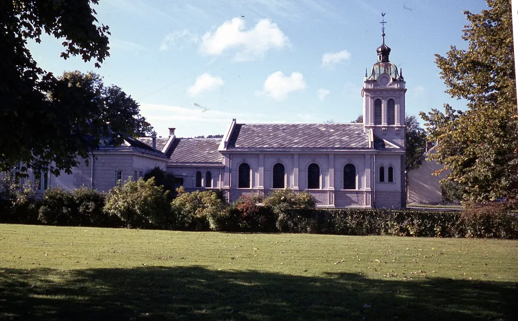 Format: Lysbilde i farge, positiv Dato / Date: Ukjent Fotograf / Photographer: Trondheim kommune, Tekniske etater/Trondheim byarkiv Sted / Place: Prinsens gate 2a, tidligere Prinsens gate 2a1 og 2a2, i dag (2018) Schirmers gate 1a, 1b og 1c, Trondheim Google Street View: <a href="https://goo.gl/maps/txAvqbXvqwC2" rel="noreferrer nofollow">goo.gl/maps/txAvqbXvqwC2</a> Wikipedia: <a href="https://no.wikipedia.org/wiki/St._Olav_domkirke_(Trondheim)" rel="noreferrer nofollow">St. Olav domkirke (Trondheim)</a> Wikipedia: <a href="https://no.wikipedia.org/wiki/Axel_Guldahl" rel="noreferrer nofollow">Axel Guldahl</a> (1866-1921) Eier / Owner Institution: Trondheim byarkiv, The Municipal Archives of Trondheim Arkivreferanse / Archive reference: Tor.H47.B59.F27228 St. Olavs kirke, Prinsens gate 2a (tidl. nr. 2aI-II), sognekirke for den katolske menighet i Trondheim (se: katolske kirke), med prestekontor, prestebolig og et mindre klosteranlegg, innviet 1974; 180 sitteplasser. Kirken ble oppført 1972-74 (ark. Per Kartvedt), og vigslet på 100-årsdagen for gjenopprettelsen av en katolsk menighet i Trondheim. Kirken eier en serie malerier av Håkon Bleken, "Korsvei", og alterveggen er utsmykket av samme kunstner. Kirken har også et vakkert krusifiks. Det finnes også en statuett av St. Margrethe av Skottland, en gave fra biskop Conti av Aberdeen til olsok 1993. Kirken eier dessuten en Mariafigur i hvit marmor av Torbjørn Skjølsvik, som ikke er fullført, og skal stå delvis ufullført. Kirken eier en relikvie av St. Olav, og er innviet til ham. Den har to klokker. Kirken ligger på den tidligere eiendommen Tønseths hage, hvor byens første jernbanestasjon lå 1864-83 (se: jernbanestasjonen, den gamle). En del av eiendommen ble kjøpt av den katolske menigheten 1897, og det tidligere lokomotivverkstedet ble ombygd til kirke (ark. Axel Guldahl sen.), og vigslet 1903. Denne kirken ble revet 1972 for å gi plass til den nåværende kirken. Bispeboliger. [...] 