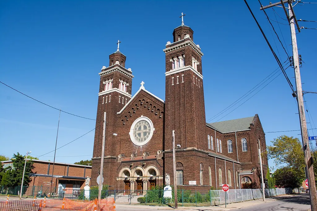 Parish hall (left) and church (right) of St. Casimir Church, located at 8223 Sowinski Avenue in Cleveland, Ohio, in the United States. St. Casimir Parish was erected in 1892. In 1894, a two-story brick structure was built on the southeast corner of Pulaski Avenue and E. 82nd Street. The church occupied the first floor, and a parochial school the second. Between 1903 and 1911, a rectory was built opposite the church on E. 82nd Street (where the convent now stands). Construction of a new, $150,000 church structure began in June 1918. It was designed by local architect William Jansen in the "Polish Cathedral style", a mixture of Romanesque Revival and vernacular architecture unique to the Midwest region. The first floor of the old building was converted for use by the school. Between 1924 and 1934, a new rectory was built, a new convent erected on the site of the old rectory, stained glass windows for the church purchased, bells for the church obtained, and the rest of the block purchased for expansion. The original church was demolished in 1948 and a new school completed in 1949. A new convent was built in 1955, and a new parish hall in 1962. The school closed in 1976, and the convent about 1982. (It is not clear if the convent is in use as of 2017.) In 2009, the Diocese of Cleveland attempted to close St. Casimir Church as part of a diocese-wide closure of more than 50 parishes. Members of the parish appealed to the Vatican, which overturned the closure. St. Casimir Church reopened in 2010. In 2017, St. Casimir Church began an extensive construction project to build rainwater catchments beneath most of its property as part of an effort to transform its campus into a "green" facility.