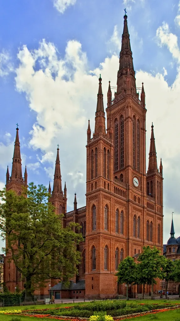 Das Bild zeigt die neugotische Marktkirche in Wiesbaden mit ihren fünf Türmen. Rechts im Bildrand ist das Neue Rathaus zu sehen. Jenseits des Neuen Rathauses befindet sich der Schlossplatz.