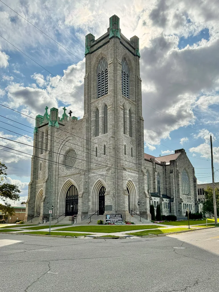 Built in 1911-1913, this Gothic Revival-style building was designed by Edwyn A. Bowd for the congregation of St. Mary Catholic Church, founded in 1866, and became the seat of the Diocese of Lansing when it was created in 1937. The building is clad in rough-hewn stone with a gabled red terra cotta tile roof, stone buttresses, gothic arched bays, rose windows, stained glass windows, front towers of varying heights with belfries featuring louvers and crenellated parapets a semi-circular rear apse, and gothic arched front entrance portals. The building was listed on the National Register of Historic Places in 1990. Today, the building remains in use as St. Mary Cathedral, the seat of the Diocese of Lansing.