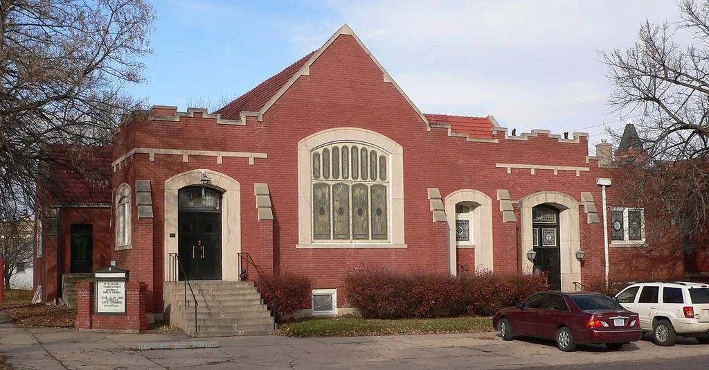 United Brethren Church building in Aurora, Nebraska, seen from the south. The building was designed in Tudor Revival style by architects "Mr. Blair" and Harvey Wood, and built in 1912. It is listed in the National Register of Historic Places. The building is no longer used as a church; it is currently occupied by L'eglise Art Center &amp; Gallery.