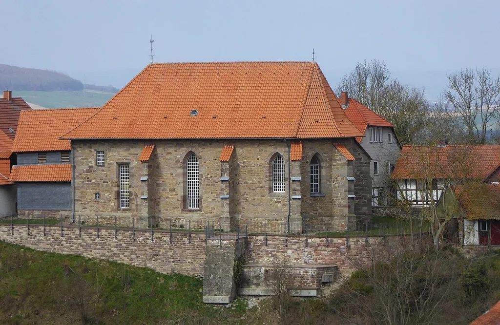 Südostansicht der Kirche St. Oswald in Bühle, Stadt Northeim, Südniedersachsen, mit der Stützmauer der Kirchhof-Einfriedung.