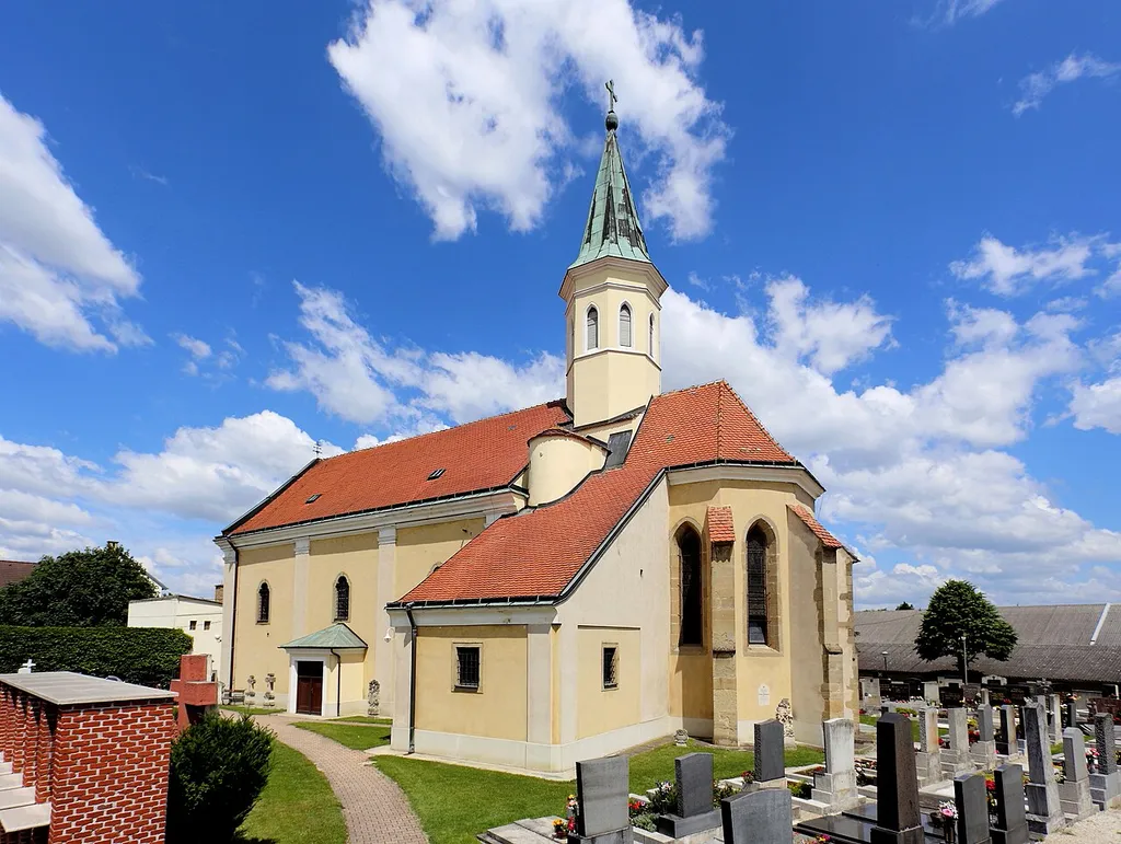 Südostansicht der Pfarrkirche Mariae Himmelfahrt in der niederösterreichischen Gemeinde Markgrafneusiedl. Eine große, im Kern (insbesondere Chor) gotische Kirche, die 1753 im barocken Stil umgebaut wurde (Neuerrichtung des Langhauses?) und von einem Friedhof umgeben ist.