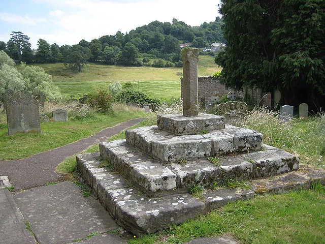 Churchyard cross, St Giles' Church, Goodrich. Remains of a cross with stepped base and a short length of an octagonal shaft with initials TW and WB and a date, 1692. A plaque is attached which reads, 'Restored in commemoration of King George V Coronation 1911.' In the distance, the lower slopes of Coppet Hill.